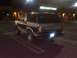 1986 Ford Bronco - A two-tone dark blue and silver Ford Bronco is parked in a lot at night, with a sign for BBQ Grill Outlet visible.
