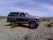 1986 Ford Bronco - This two-tone Ford Bronco is parked on a rocky, arid terrain under a partly cloudy sky.