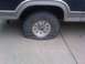 1986 Ford Bronco - A flat tire is visible on the side of a 1986 Ford Bronco.