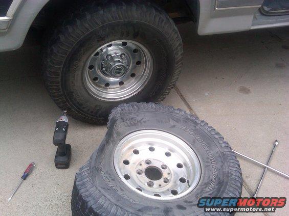Flat tire on a vehicle, with a spare tire, lug wrench, screwdriver, and drill nearby
