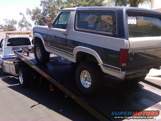 Two-tone gray and dark blue Ford Bronco on a flatbed tow truck, rear quarter view. "000" sticker on rear window