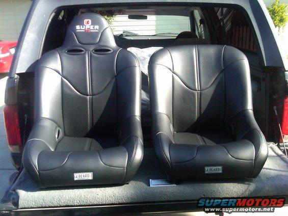 Two black racing seats with 'SUPER' logo on headrest and 'J BEARD' plates on base, placed in truck bed