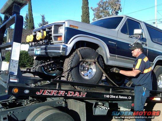 Two-tone gray and blue Ford Bronco on a Jerr-Dan tow truck, front passenger side visible