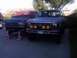 1986 Ford Bronco - Two Ford Broncos are parked in a driveway. The front one has four smiley face auxiliary lights mounted on its bumper.