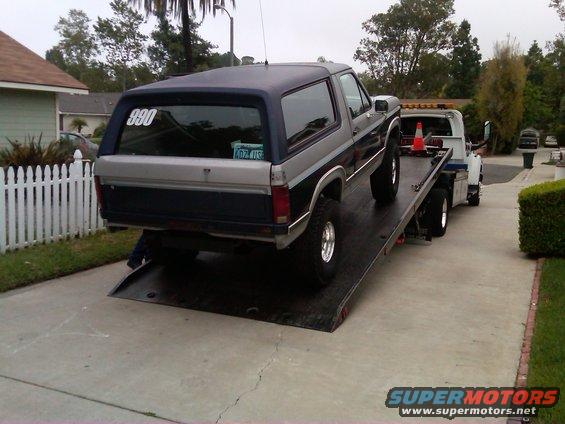 Two-tone gray and blue Ford Bronco being towed on a flatbed truck