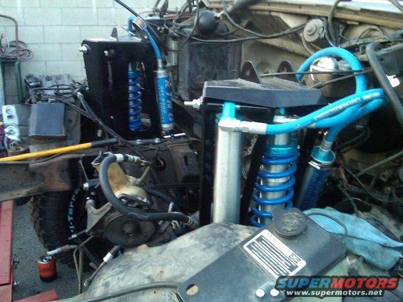 Custom off-road suspension with blue coilover shocks and hydraulic lines. Part of a vehicle's engine bay