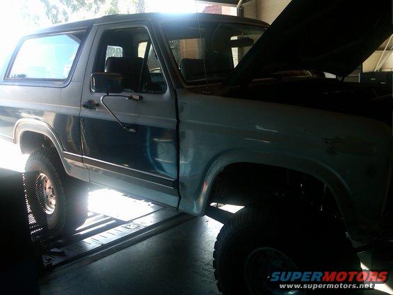 Ford Bronco with hood up, parked on a lift inside a garage