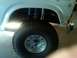 1986 Ford Bronco - Close-up of the front wheel and fender of a 1986 Ford Bronco, showing off its suspension and tire.