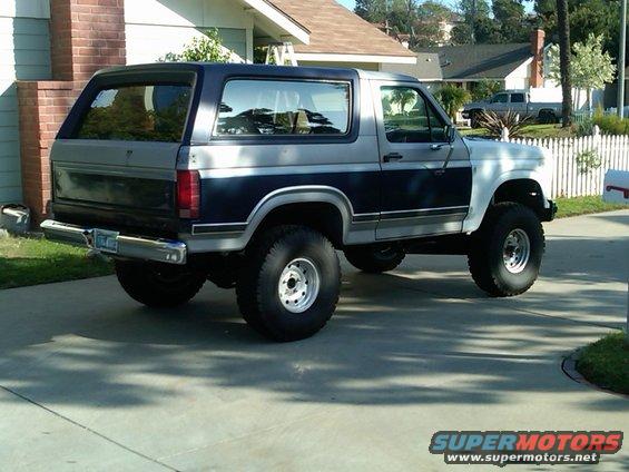 Ford Bronco parked in a driveway, side and rear view. It has a two-tone paint job with blue and silver