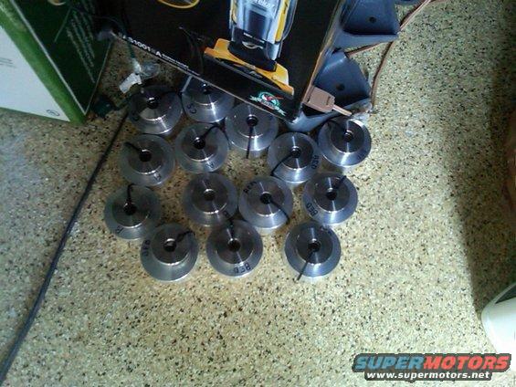 Pile of circular metal parts with black ties, some marked 'BED' and '038', on a speckled floor next to a box