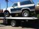 1986 Ford Bronco - A white and blue Ford Bronco is loaded onto a flatbed tow truck.