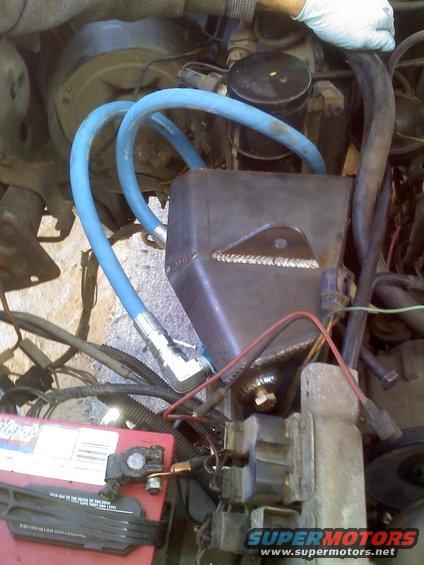 Close-up of engine bay with blue hoses, a metal box, and a battery