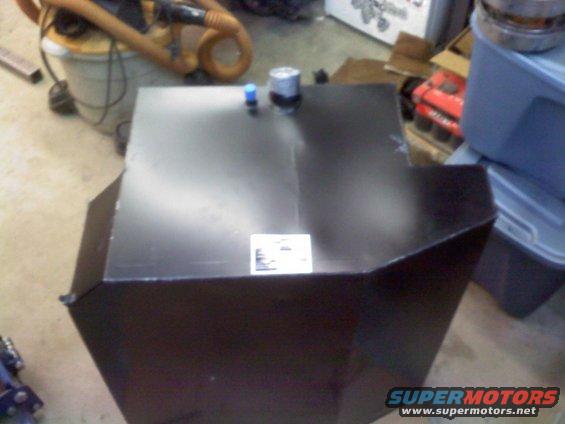 Black fuel tank with two caps on top, sitting on a concrete floor with a shop vac in the background