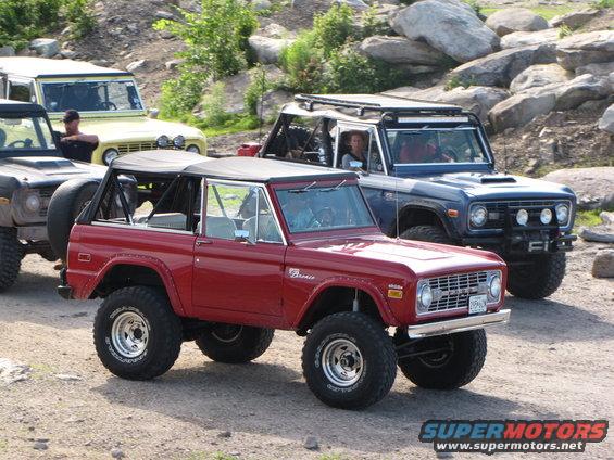 Red Ford Bronco with a black soft top, lifted suspension, and off-road tires