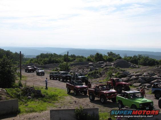 Several Ford Broncos and other off-road vehicles parked on a dirt path with a scenic mountain view