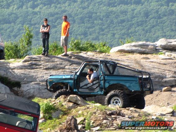 Teal off-road SUV with roll cage navigating rocky terrain