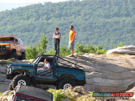 Teal 1979 Ford Bronco with roll cage on rocky terrain