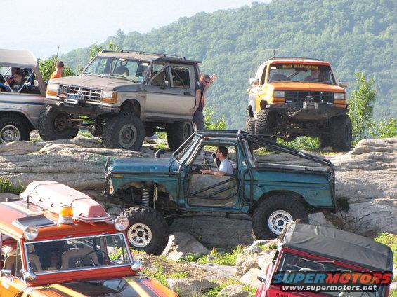 Multiple off-road vehicles, including a 1979 Ford Bronco, navigating a rocky trail