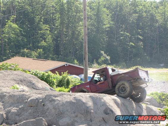 Maroon pickup truck climbing over large rocks on a trail, driver visible inside