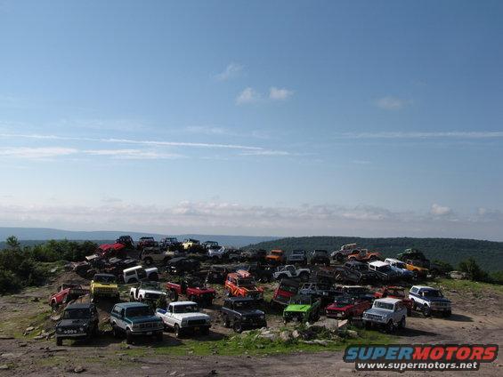 Many off-road vehicles parked on a rocky hill under a blue sky. Includes Broncos, Jeeps, and other 4x4s