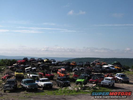 Many Ford Broncos and other SUVs parked on a rocky hillside under a blue sky