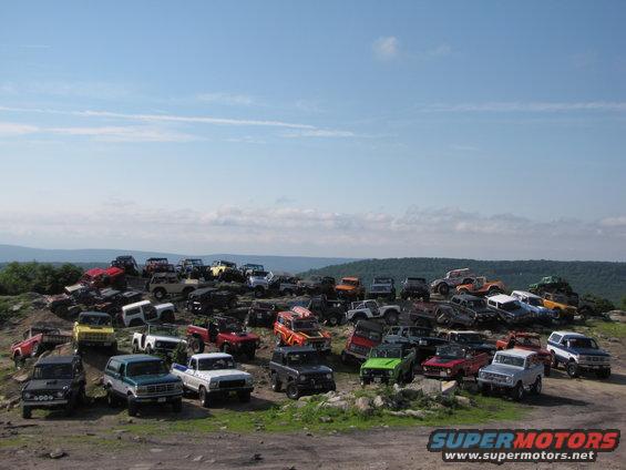 Many Ford Broncos and other SUVs parked on a hill under a blue sky
