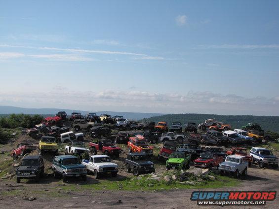 Many off-road vehicles parked on a rocky hill under a blue sky