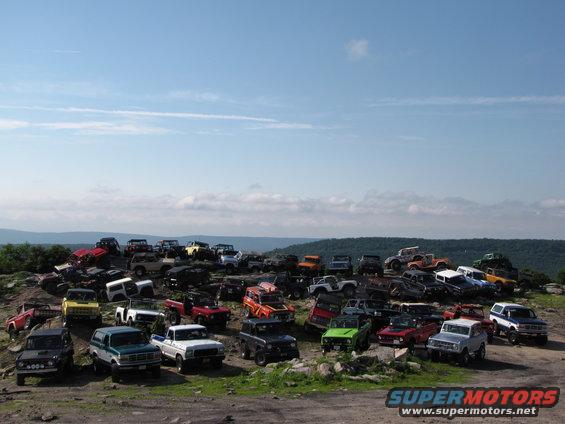 Many Ford Broncos and other SUVs parked on a rocky hillside under a blue sky