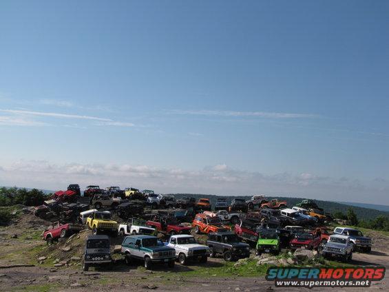 Many SUVs and trucks parked on a rocky hill under a blue sky