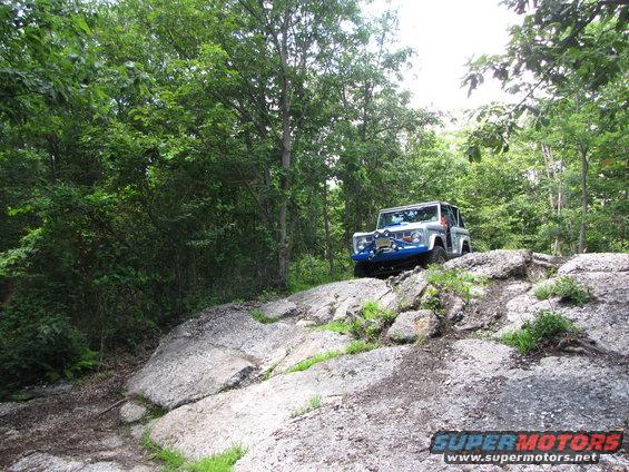 Silver off-road vehicle with blue bumper guards climbing a rocky hill