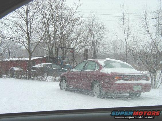 red sedan parked in snow, another car in background