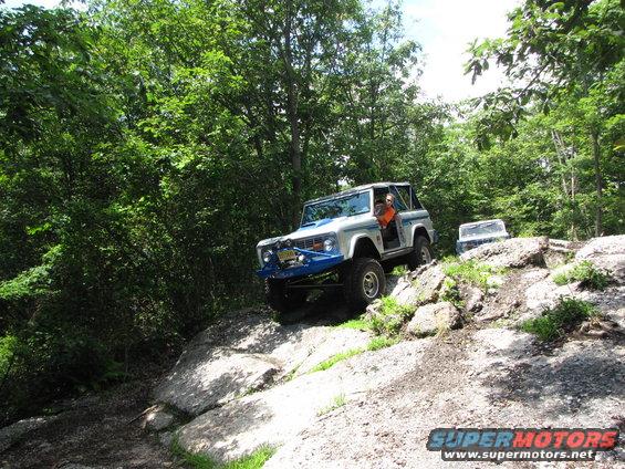 White Ford Bronco with blue bumper climbing rocks