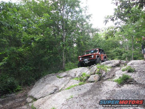 orange SUV climbing rocky trail, trees all around