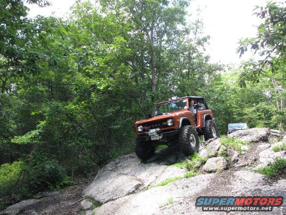 Orange off-road SUV with large tires climbing rocks, winch on front bumper, soft top