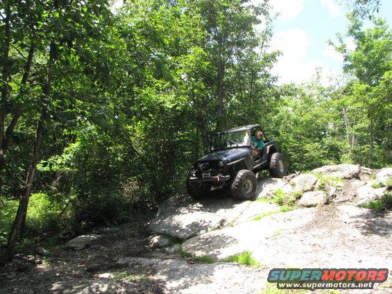 Black Jeep Wrangler climbing over large rocks on a wooded trail