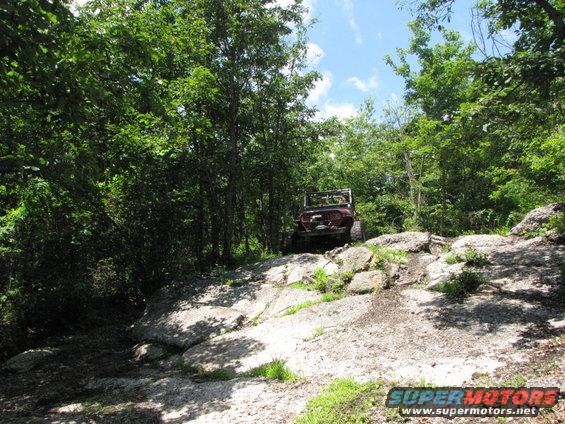 red Jeep climbing rocky trail in woods