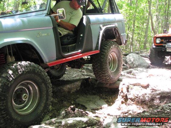 Two off-road vehicles navigating a rocky trail, one is a light blue SUV with red trim