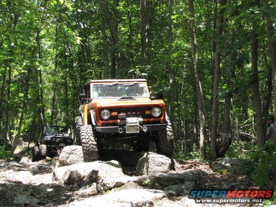 Orange 1978 Ford Bronco off-roading over rocks, front winch visible