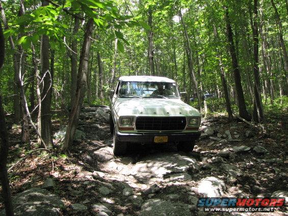 White 1978 Ford Bronco driving on a rocky, wooded trail