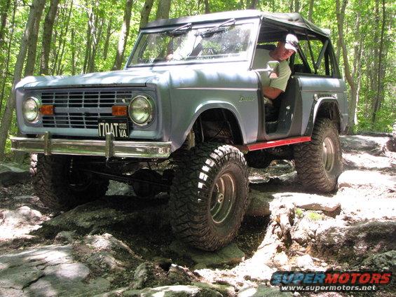 Light blue 1977 Ford Bronco with off-road tires navigating rocky terrain. Driver visible