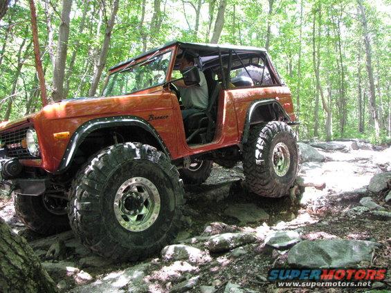 1979 Ford Bronco with large off-road tires navigating a rocky trail in a wooded area