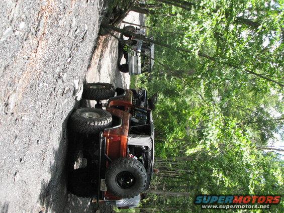 Orange off-road SUV with large tires on a dirt path, another vehicle behind
