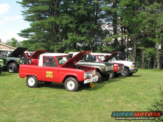 Red 1978 Ford Bronco with white top and hood open, parked on grass with other vehicles