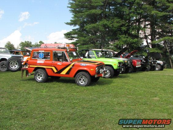 Orange 1979 Ford Bronco with yellow stripes and emergency star emblem parked in a line of vehicles