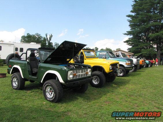 Green 1978 Ford Bronco with hood open, parked in a line with other trucks and SUVs on grass