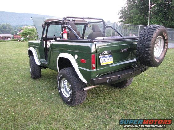 Green Ford Bronco, rear view, with spare tire mounted on swing-away carrier. Hood is open