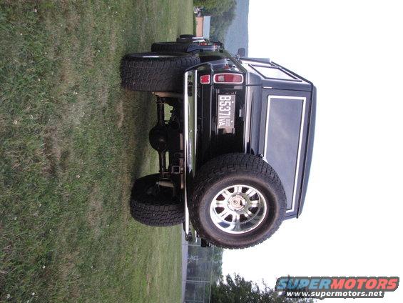 Black SUV's rear quarter view shows large tires, chrome bumper, and license plate B537IVA