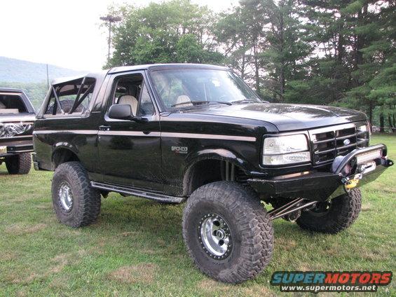 Black lifted Ford Bronco with aftermarket bumper and light bar. Another Bronco is partially visible to the left