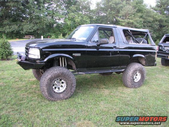 Lifted black Ford Bronco with large tires and custom bumper parked on grass