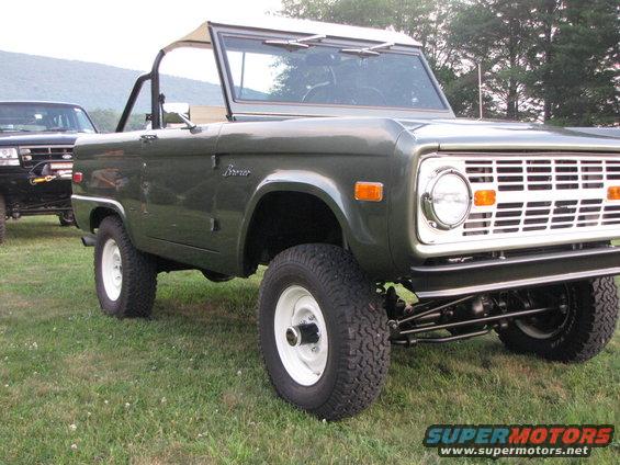 Green Ford Bronco parked on grass, another black SUV behind it